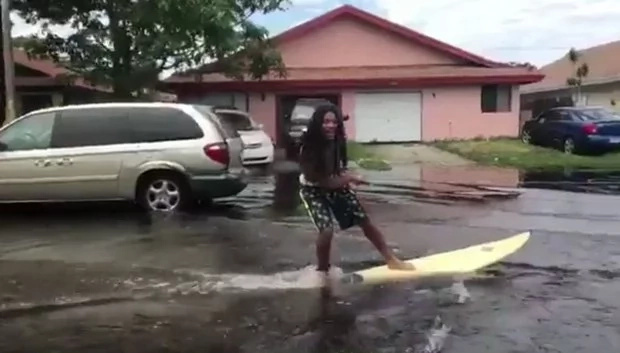 Man gets on his surfboard on flooded street Man gets on his surfboard on flooded street