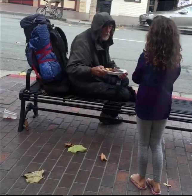 Adorable young girl shares her dinner with homeless man outside restaurant Adorable young girl shares her dinner with homeless man outside restaurant